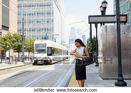 Stock Photography - Businesswoman checking time by light rail line. Fotosearch