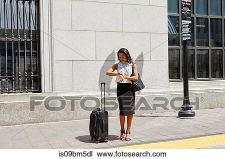 Stock Image - Businesswoman checking time on kerb. Fotosearch