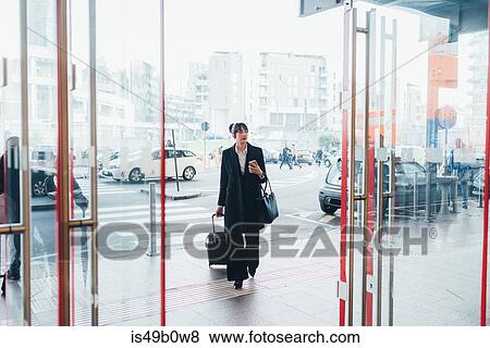 Businesswoman pulling trolley luggage into building, Milan, Italy View Large Photo Image Stock Photo - Businesswoman pulling trolley luggage into building, Milan, Italy. Fotosearch