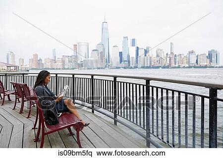 Stock Photography - Businesswoman reading newspapers, New York City skyline in background. Fotosearch