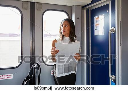 Stock Image - Businesswoman reading newspapers on train. Fotosearch