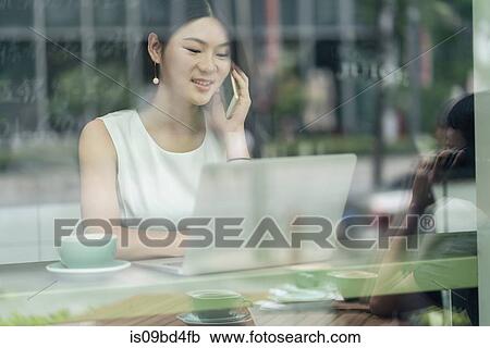 Businesswoman sitting in cafe, using smartphone and laptop, viewed through window View Large Photo Image Stock Image - Businesswoman sitting in cafe, using smartphone and laptop, viewed through window. Fotosearch