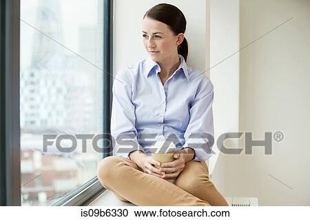 Businesswoman sitting on window ledge, looking out of window, holding takeaway coffee cup View Large Photo Image Stock Image - Businesswoman sitting on window ledge, looking out of window, holding takeaway coffee cup. Fotosearch