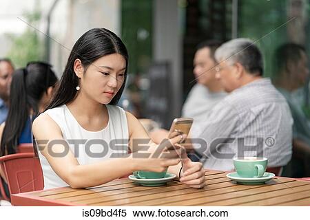 Businesswoman sitting outdoors, at cafe, using smartphone View Large Photo Image Stock Photography - Businesswoman sitting outdoors, at cafe, using smartphone. Fotosearch