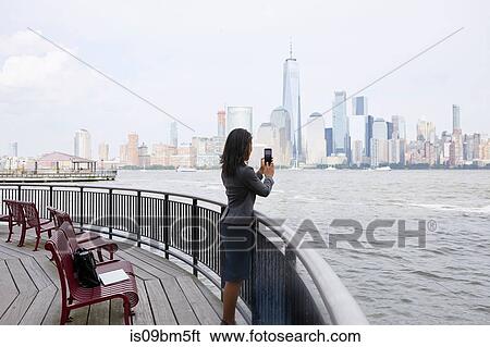 Stock Photograph - Businesswoman taking photograph of New York City skyline. Fotosearch