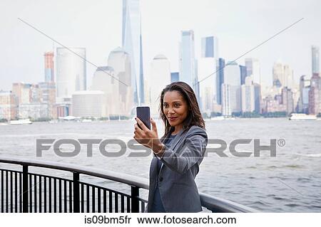 Businesswoman taking selfie, New York City skyline in background View Large Photo Image Stock Photography - Businesswoman taking selfie, New York City skyline in background. Fotosearch