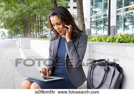 Stock Photo - Businesswoman using cellphone and laptop on street seating. Fotosearch