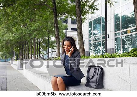 Businesswoman using cellphone and laptop on street seating View Large Photo Image Stock Photo - Businesswoman using cellphone and laptop on street seating. Fotosearch