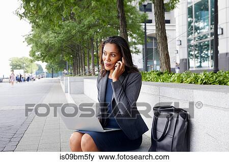 Businesswoman using cellphone and laptop on street seating View Large Photo Image Stock Photo - Businesswoman using cellphone and laptop on street seating. Fotosearch
