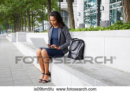 Businesswoman using cellphone and laptop on street seating View Large Photo Image Stock Photograph - Businesswoman using cellphone and laptop on street seating. Fotosearch