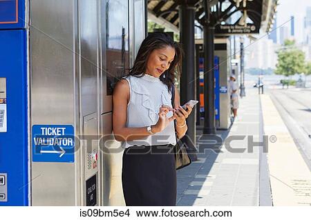 Picture - Businesswoman using cellphone by ticket machine. Fotosearch