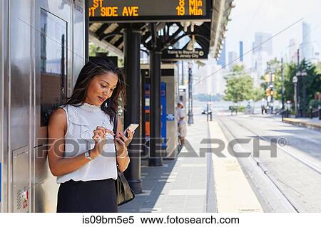 Stock Photography - Businesswoman using cellphone by ticket machine. Fotosearch