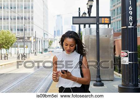 Stock Image - Businesswoman using cellphone in street. Fotosearch