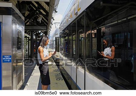 Stock Image - Businesswoman using cellphone in train station. Fotosearch