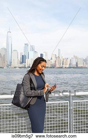 Businesswoman using cellphone, New York City skyline in background View Large Photo Image Stock Photo - Businesswoman using cellphone, New York City skyline in background. Fotosearch