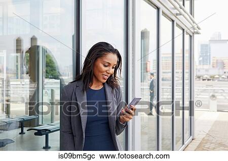 Stock Image - Businesswoman using cellphone outside ferry terminal. Fotosearch