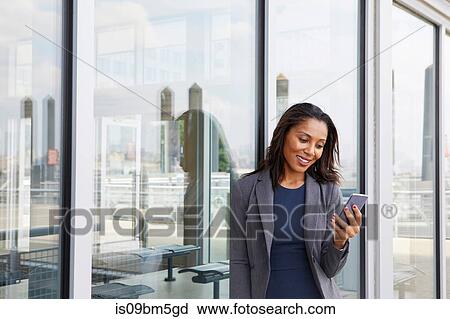 Stock Image - Businesswoman using cellphone outside ferry terminal. Fotosearch