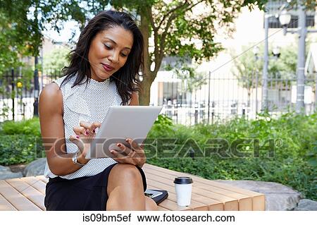 Stock Image - Businesswoman using digital tablet in park. Fotosearch