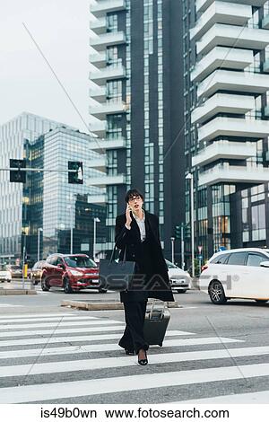 Picture - Businesswoman using mobile and pulling trolley luggage, Milan, Italy. Fotosearch