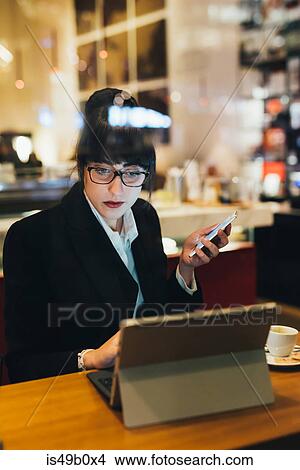 Picture - Businesswoman using mobile phone and digital tablet in cafe. Fotosearch