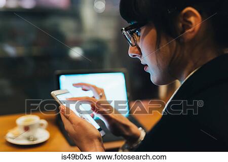 Stock Photography - Businesswoman using mobile phone and laptop in cafe. Fotosearch