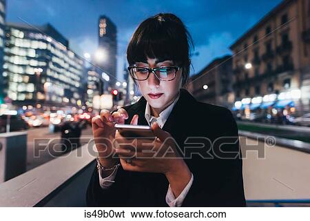 Stock Photograph - Businesswoman using mobile phone by wall on busy road, Milan, Italy. Fotosearch