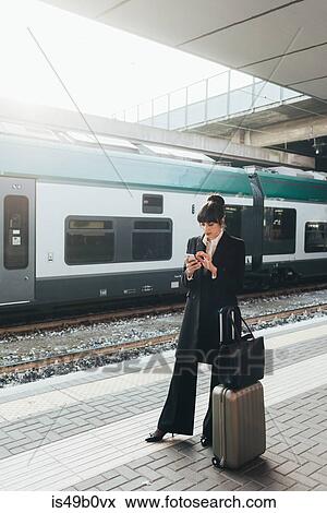 Stock Photo - Businesswoman using mobile phone in train station, Milan, Italy. Fotosearch