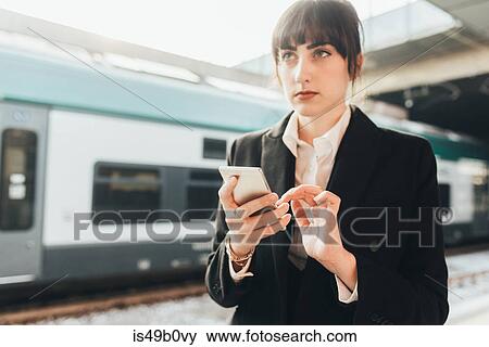 Stock Photo - Businesswoman using mobile phone in train station, Milan, Italy. Fotosearch