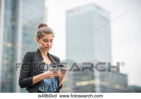 Stock Image - Businesswoman using mobile phone, Canary Wharf, London, UK. Fotosearch
