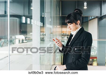 Stock Image - Businesswoman using mobile phone, Milan, Italy. Fotosearch