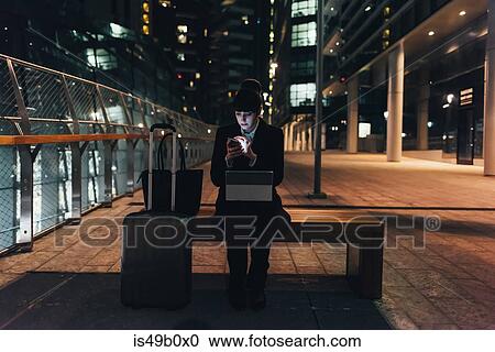 Stock Image - Businesswoman with trolley luggage using digital tablet, Milan, Italy. Fotosearch