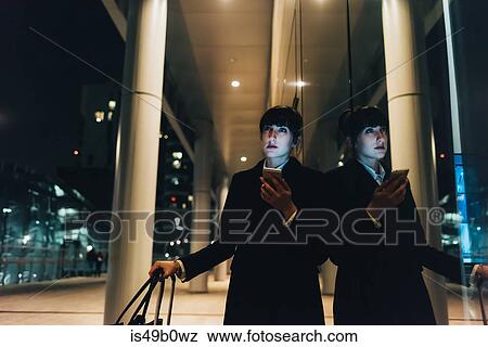 Businesswoman with trolley luggage using mobile waiting by pillars, Milan, Italy View Large Photo Image Stock Photo - Businesswoman with trolley luggage using mobile waiting by pillars, Milan, Italy. Fotosearch
