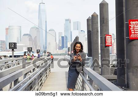 Stock Image - Businesswoman with wheeled luggage on ferry pier. Fotosearch