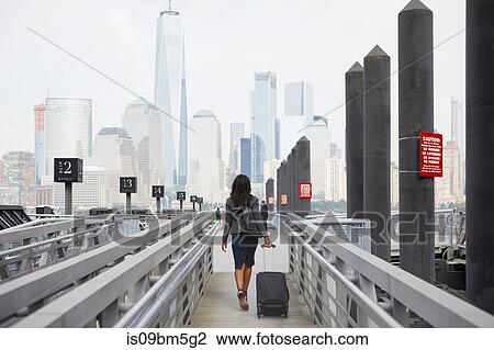 Stock Image - Businesswoman with wheeled luggage on ferry pier. Fotosearch