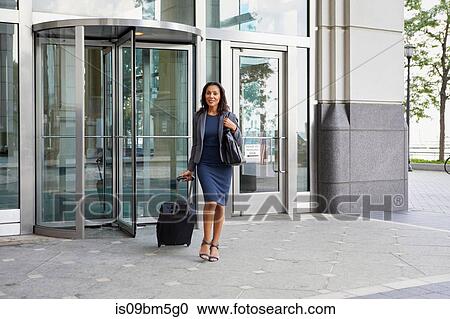 Stock Image - Businesswoman with wheeled luggage. Fotosearch