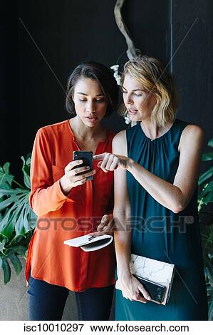 Businesswomen reading message on cellular phone View Large Photo Image Stock Photo - Businesswomen reading message on cellular phone. Fotosearch
