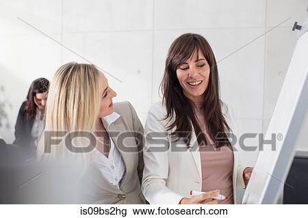 Businesswomen talking to colleague and writing on whiteboard in office View Large Photo Image Stock Image - Businesswomen talking to colleague and writing on whiteboard in office. Fotosearch