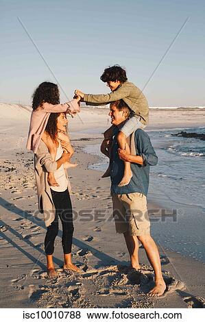 Stock Photo - Children piggyback fighting on parents at beach. Fotosearch