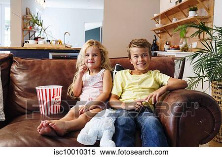 Stock Photography - Children relaxing with popcorn on sofa at home. Fotosearch