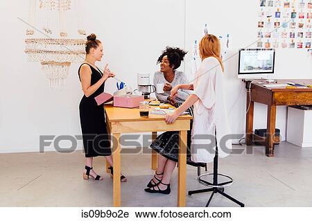 Stock Image - Colleagues in coffee area sharing box of doughnuts. Fotosearch