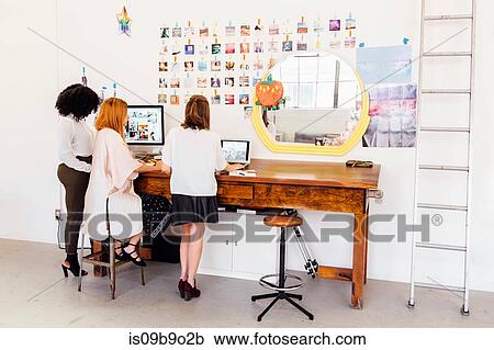 Stock Image - Colleagues in creative studio having discussion, using computer. Fotosearch