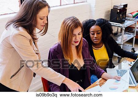 Stock Photography - Colleagues in office discussing graphical data on paperwork. Fotosearch