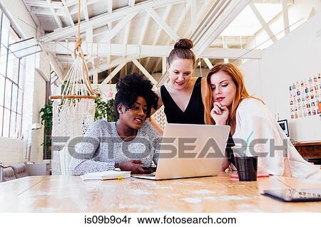 Stock Photography - Colleagues in office using laptop together. Fotosearch