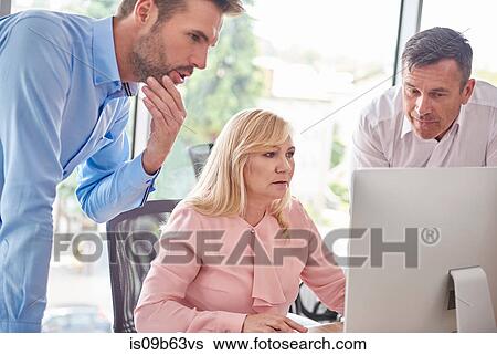 Stock Photograph - Colleagues in office with computer having discussion. Fotosearch