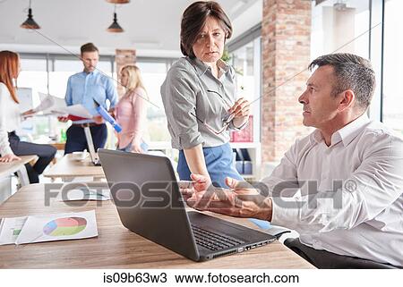Stock Image - Colleagues in office with laptop having discussion. Fotosearch