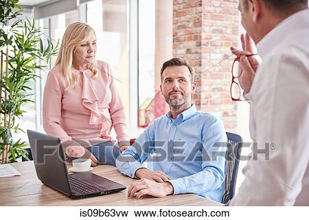 Stock Photo - Colleagues in office with laptop having discussion. Fotosearch
