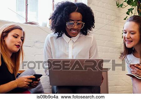 Stock Image - Colleagues sitting together on sofa in office using laptop. Fotosearch