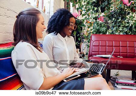 Colleagues sitting together on sofa in office using laptop View Large Photo Image Stock Photo - Colleagues sitting together on sofa in office using laptop. Fotosearch