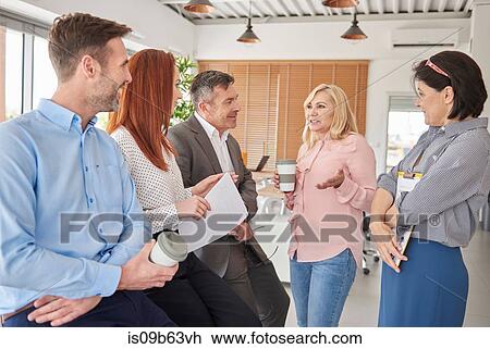Stock Image - Colleagues standing in office talking. Fotosearch