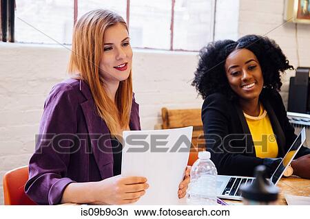 Picture - Colleagues working together at desk, looking away smiling. Fotosearch